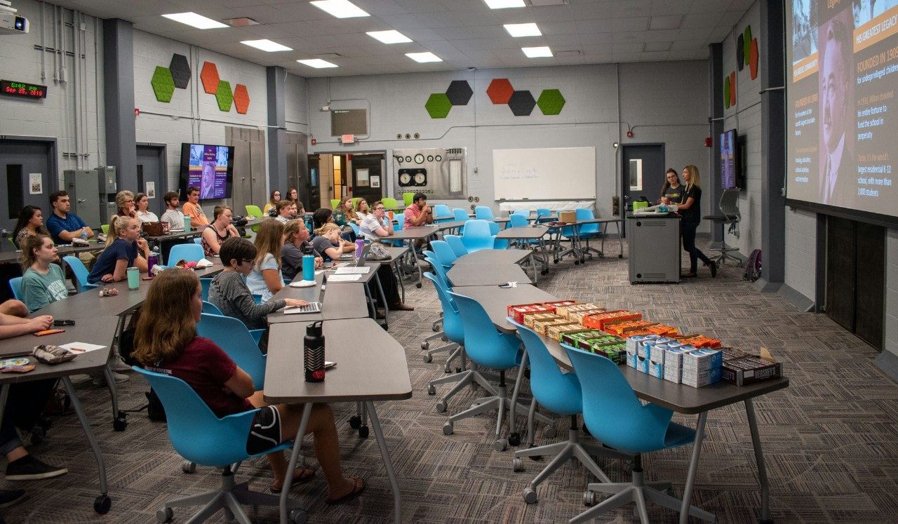 Two presenters speak to a full classroom.