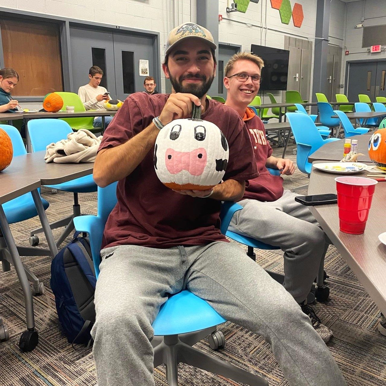 A student holds up a pumpkin painted to look like a cow's face.