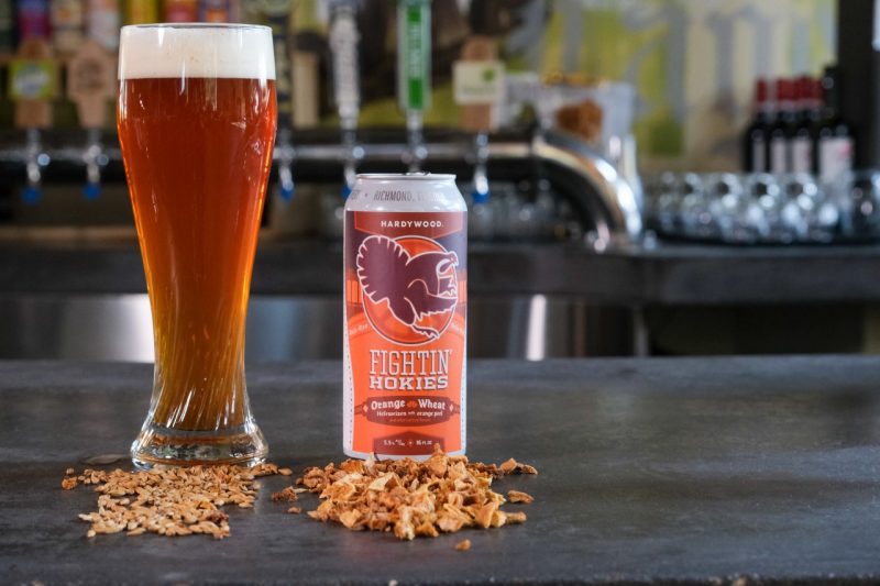 A can of Fightin' Hokies Orange Wheat next to a glass of it. The beer is a deep orange color. 