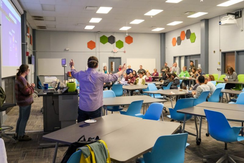 A speaker addresses a crowd of students in a large classroom