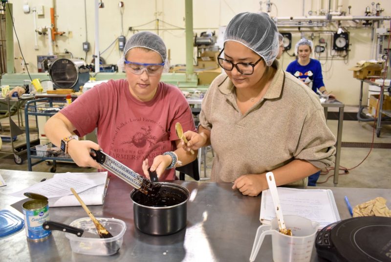 Two students work on a pot of food they're cooking to temperature
