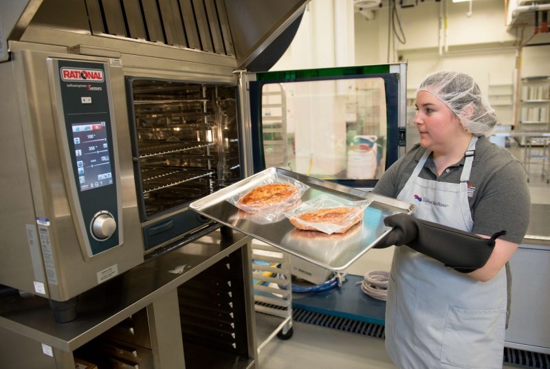A researcher inserts food into an oven in a lab