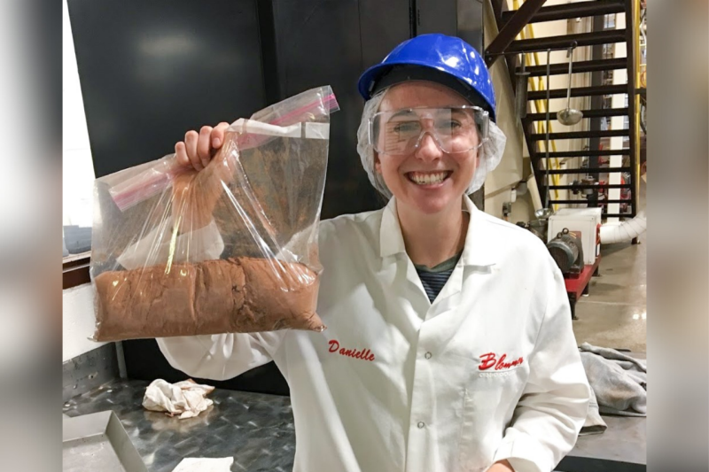 A student holds up a bag of cocoa while interning at a chocolate company