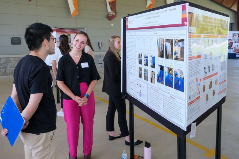 A student presents their work on a research poster to a viewer.