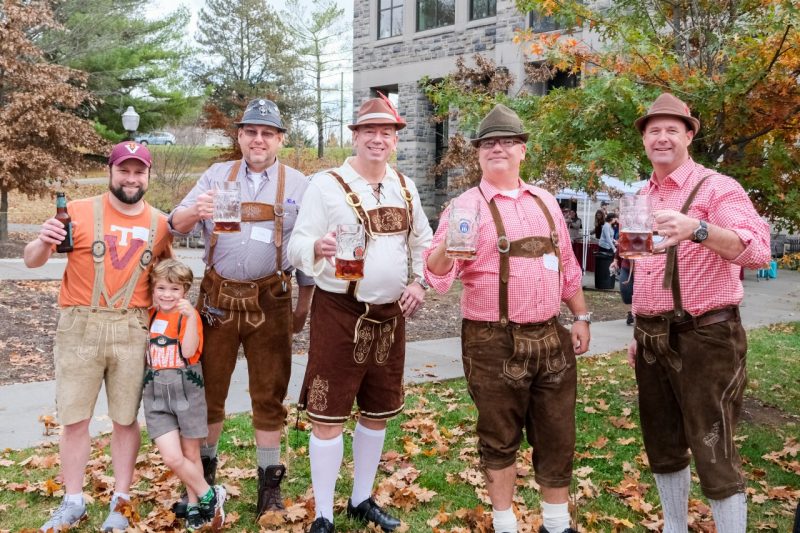 Attendees holding up their beers and dressed in lederhosen at OktoberFST 2022
